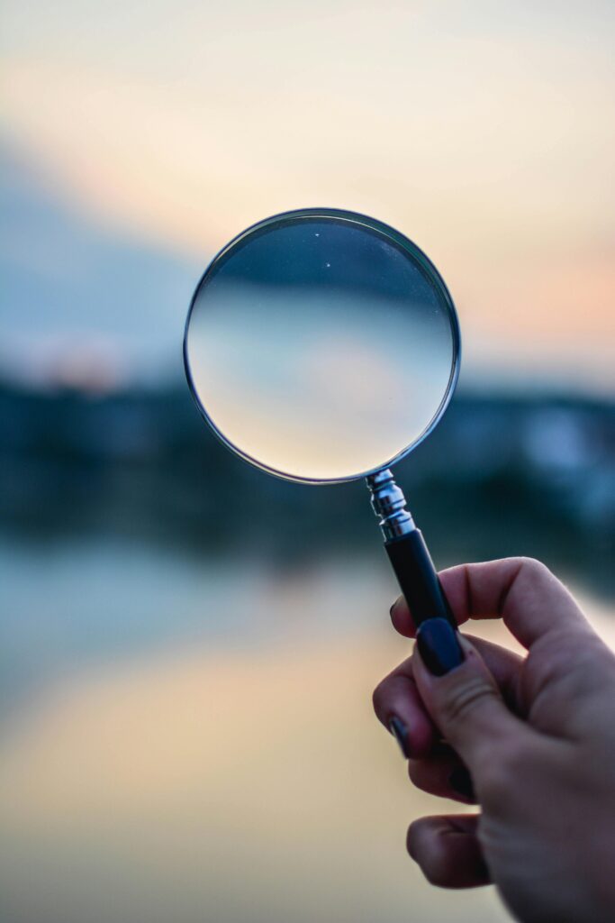 A magnifying glass held by a hand outdoors at sunset, focusing on exploration.